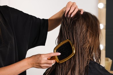 Photo of Hairdresser brushing client's wet hair in salon, closeup