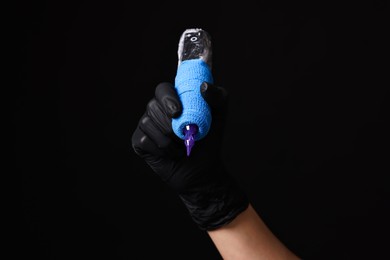 Photo of Professional artist in gloves holding tattoo machine on black background, closeup