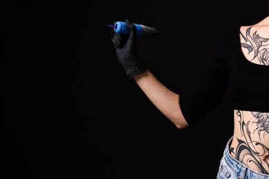 Photo of Professional artist in gloves holding tattoo machine on black background, closeup. Space for text