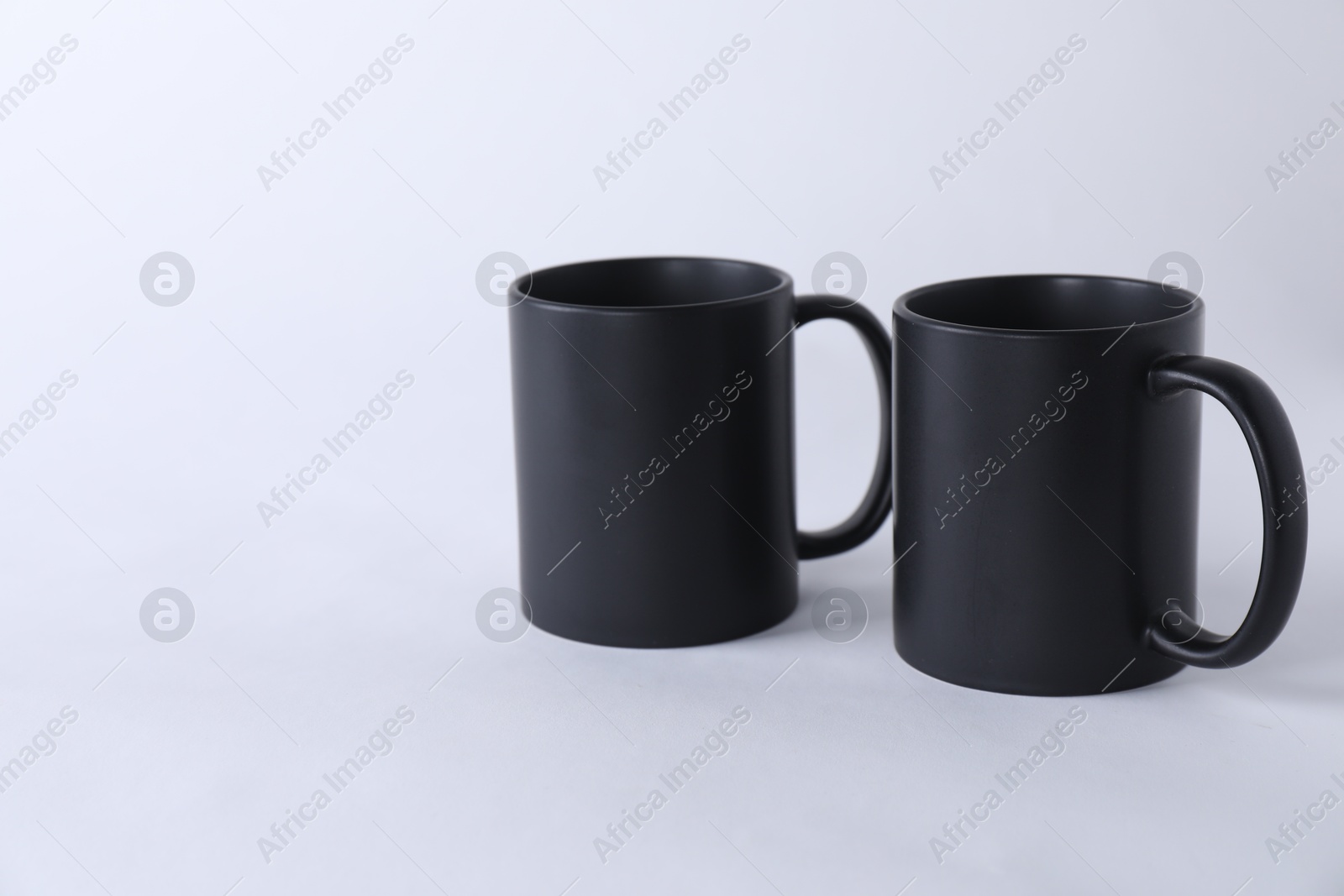 Photo of Two blank black mugs on white background. Mockup for design