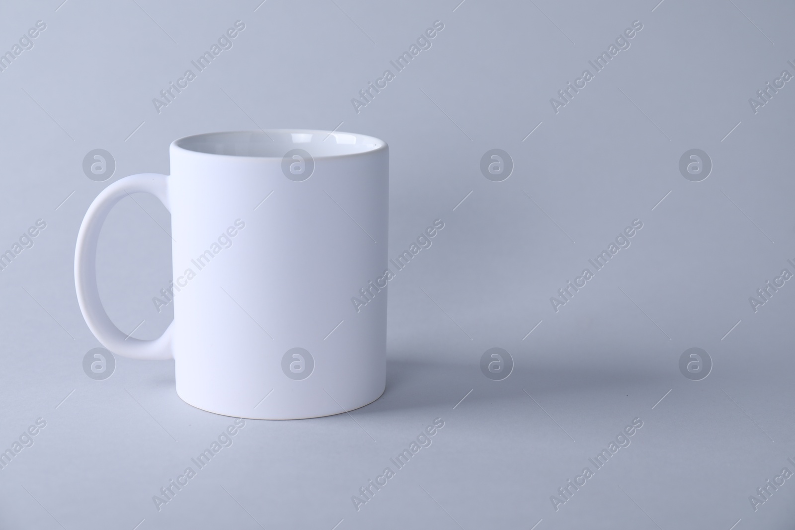 Photo of One blank white mug on light background. Mockup for design