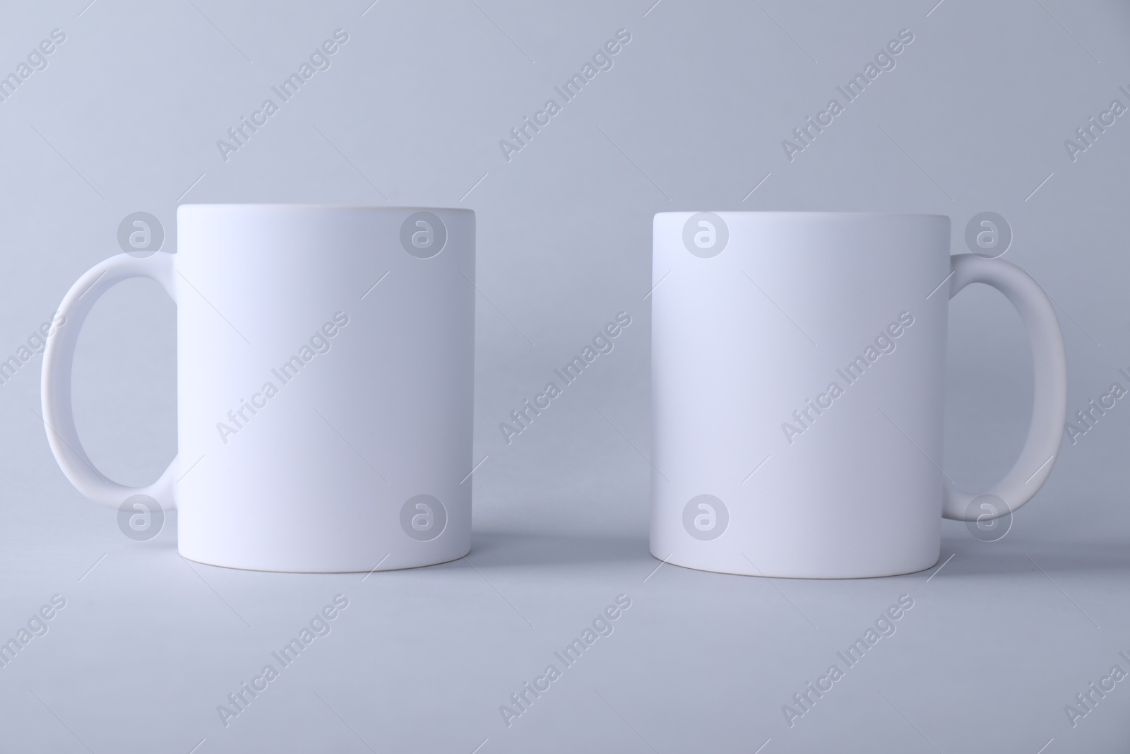 Photo of Two blank white mugs on light background. Mockup for design