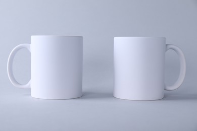 Photo of Two blank white mugs on light background. Mockup for design