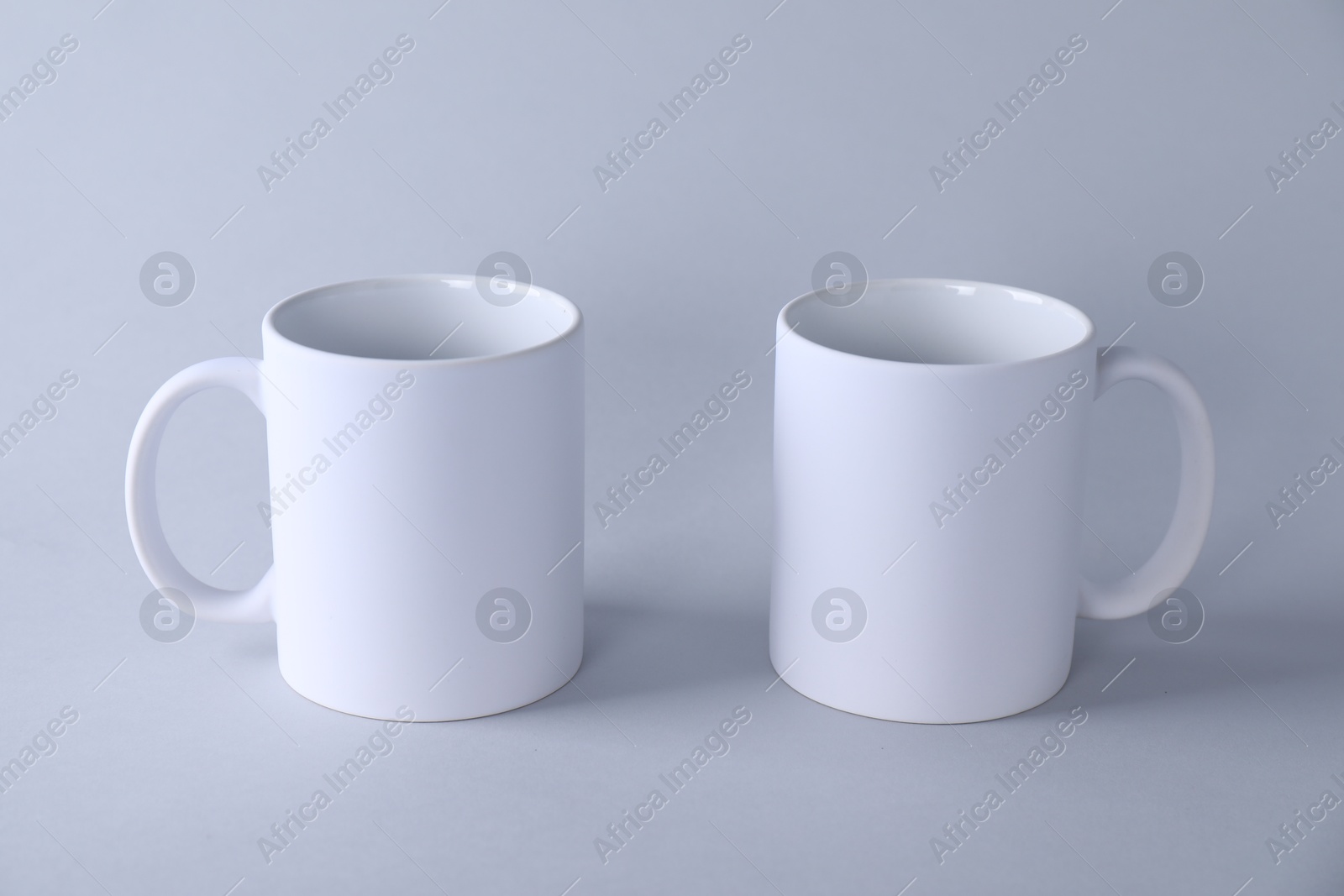 Photo of Two blank white mugs on light background. Mockup for design