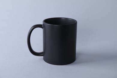 Photo of One blank black mug on light background. Mockup for design