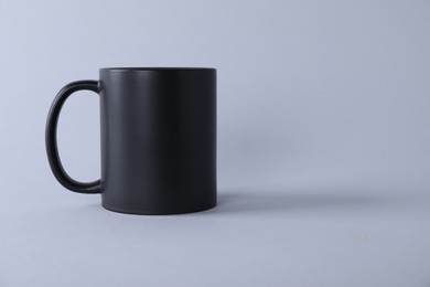 Photo of One blank black mug on light background. Mockup for design