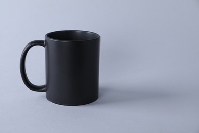 Photo of One blank black mug on light background. Mockup for design