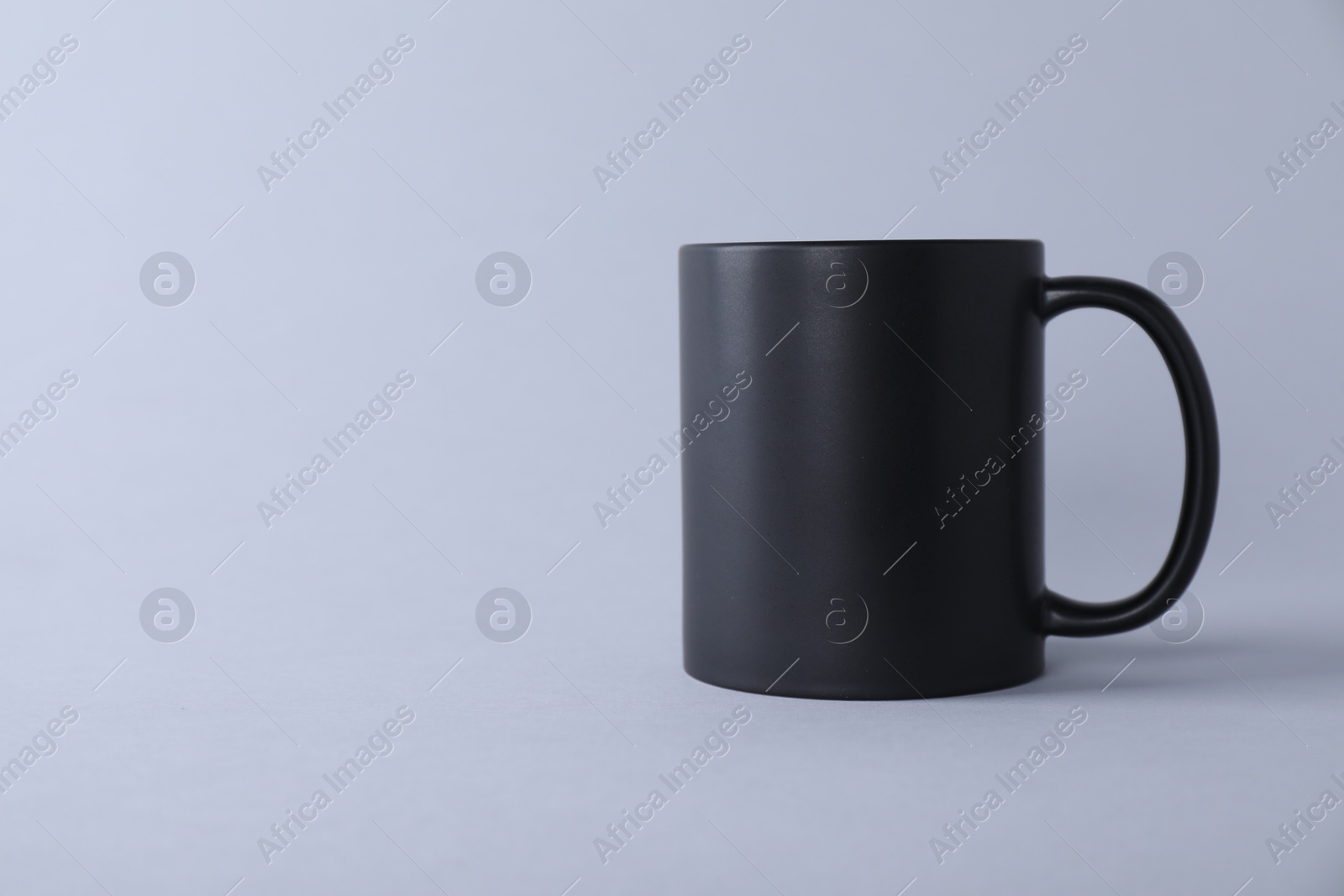 Photo of One blank black mug on light background. Mockup for design