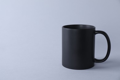 Photo of One blank black mug on light background. Mockup for design