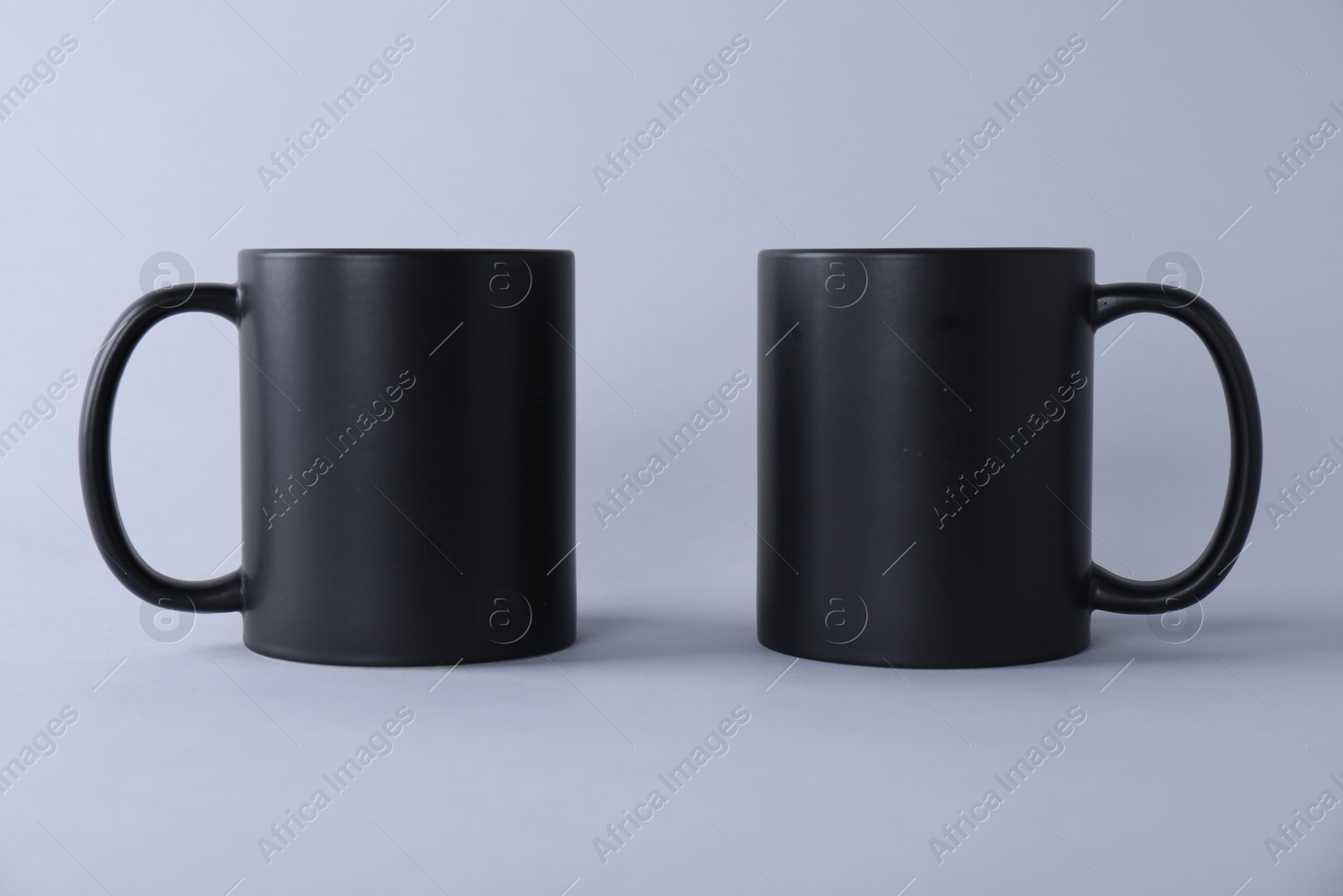 Photo of Two blank black mugs on light background. Mockup for design