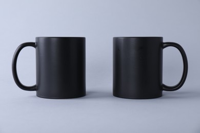 Photo of Two blank black mugs on light background. Mockup for design