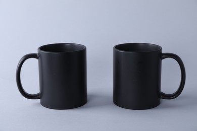 Photo of Two blank black mugs on light background. Mockup for design