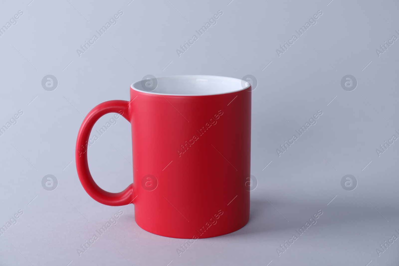 Photo of One blank red mug on light background. Mockup for design