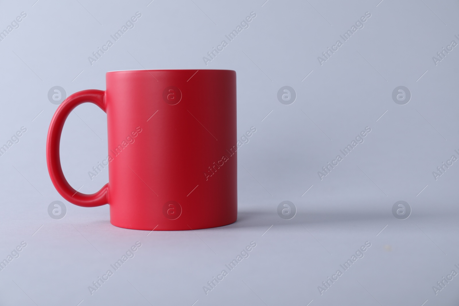 Photo of One blank red mug on light background. Mockup for design