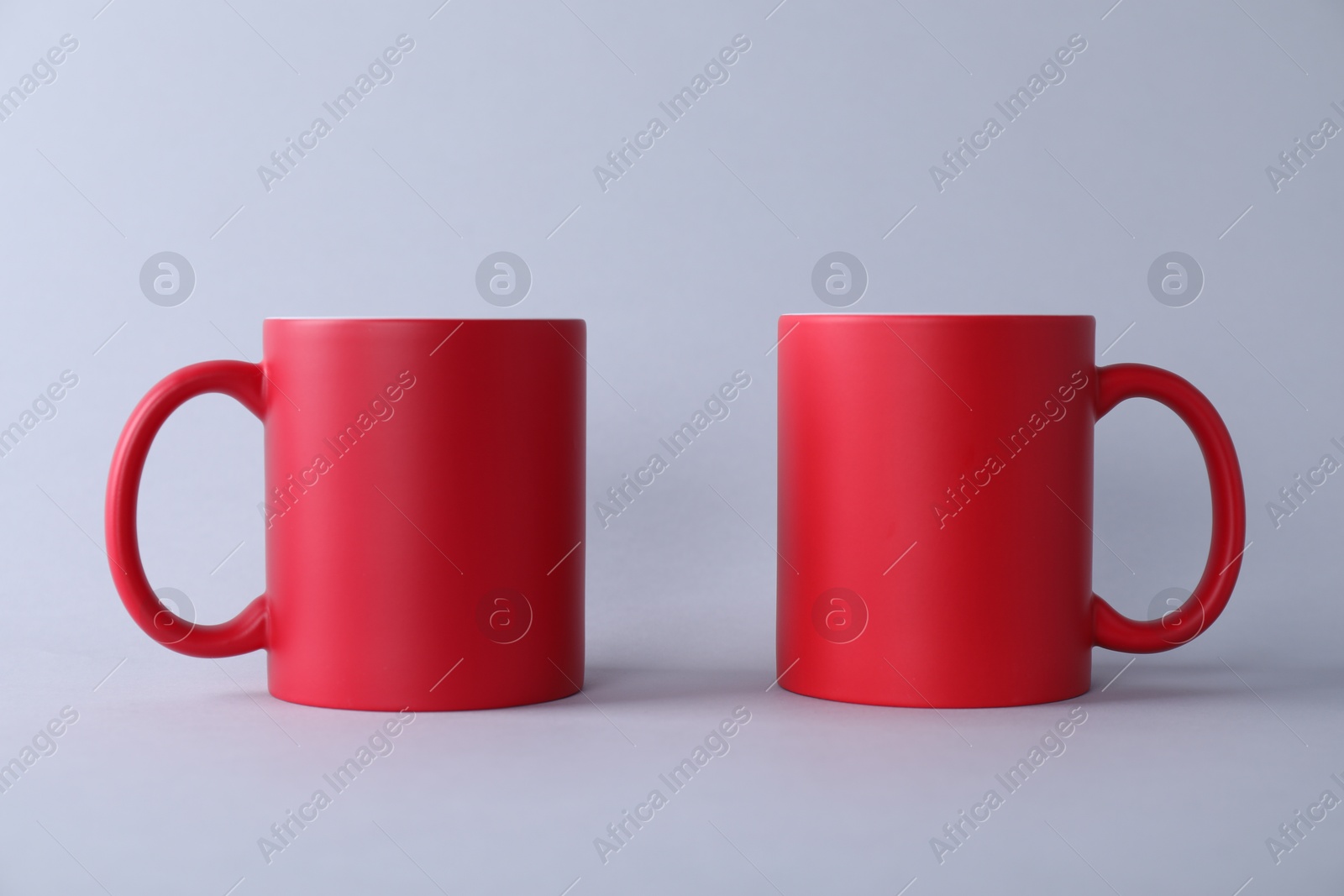 Photo of Two blank red mugs on light background. Mockup for design