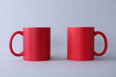 Photo of Two blank red mugs on light background. Mockup for design