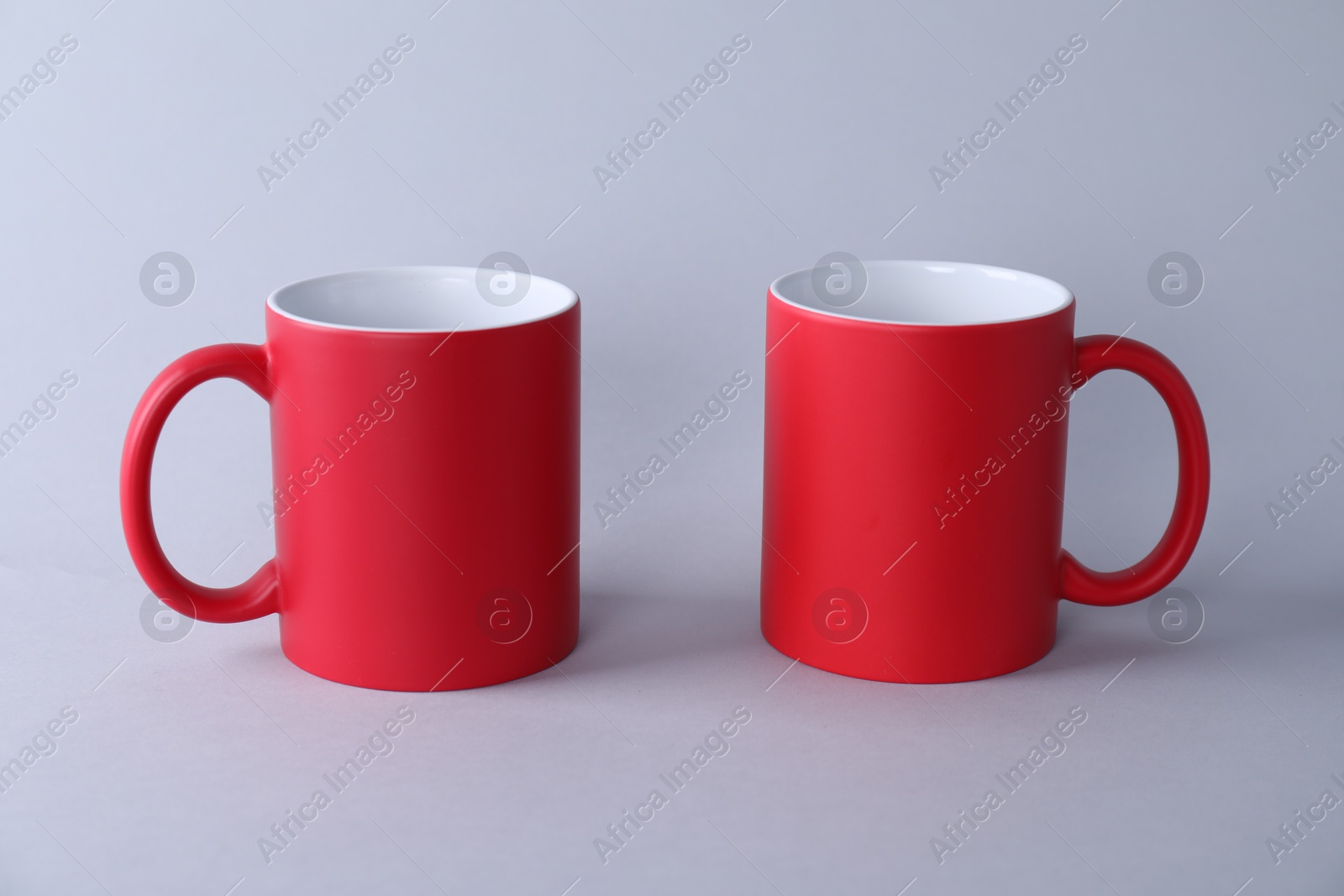 Photo of Two blank red mugs on light background. Mockup for design