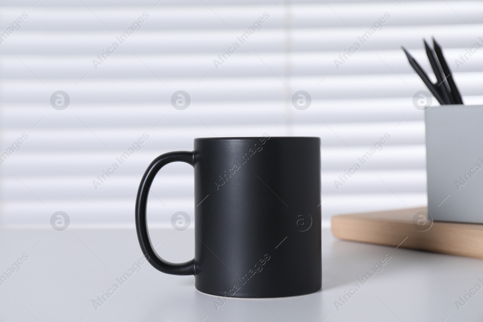 Photo of One blank black ceramic mug and stationery on white table. Mockup for design