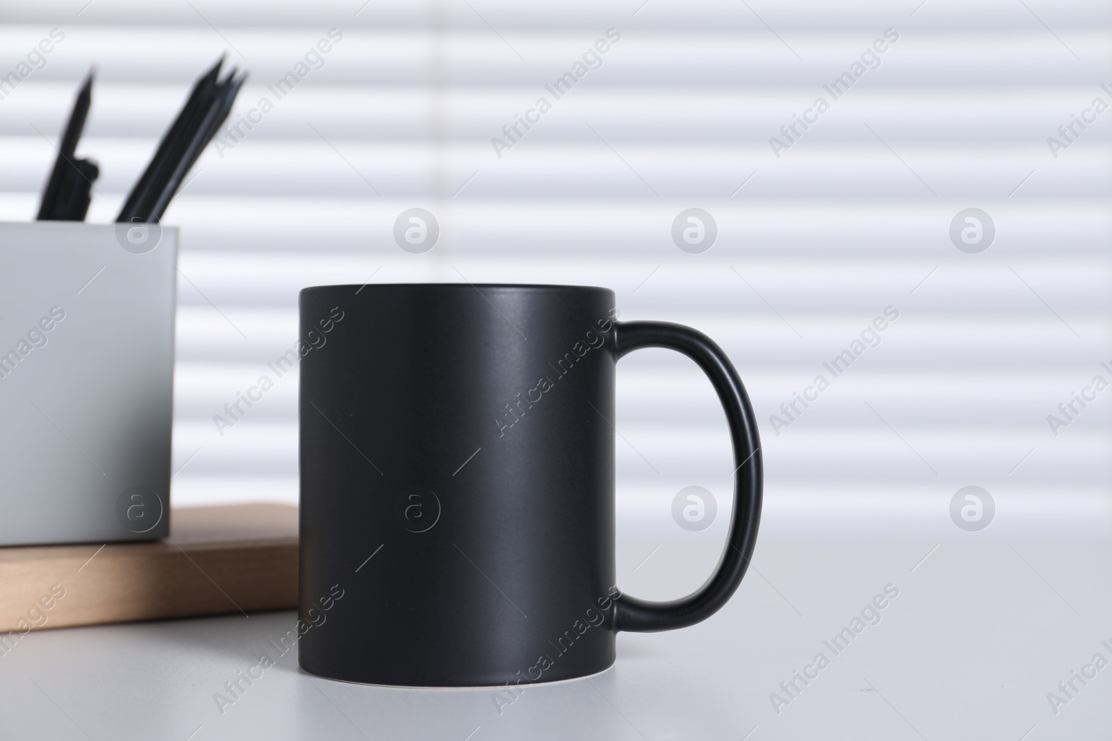 Photo of One blank black ceramic mug and stationery on white table. Mockup for design