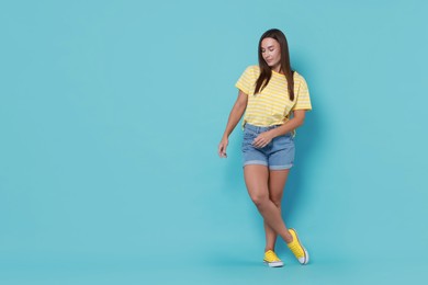 Photo of Beautiful woman wearing stylish denim shorts on light blue background, space for text