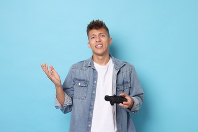 Photo of Unhappy young man with controller on light blue background