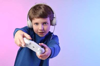 Photo of Cute little boy in headphones playing video game with controller on color background. Space for text