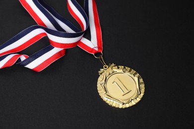 Photo of Golden medal with striped ribbon on black background, closeup