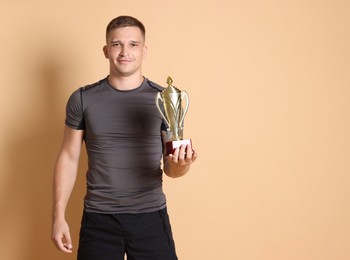 Smiling winner with golden trophy cup on beige background, space for text