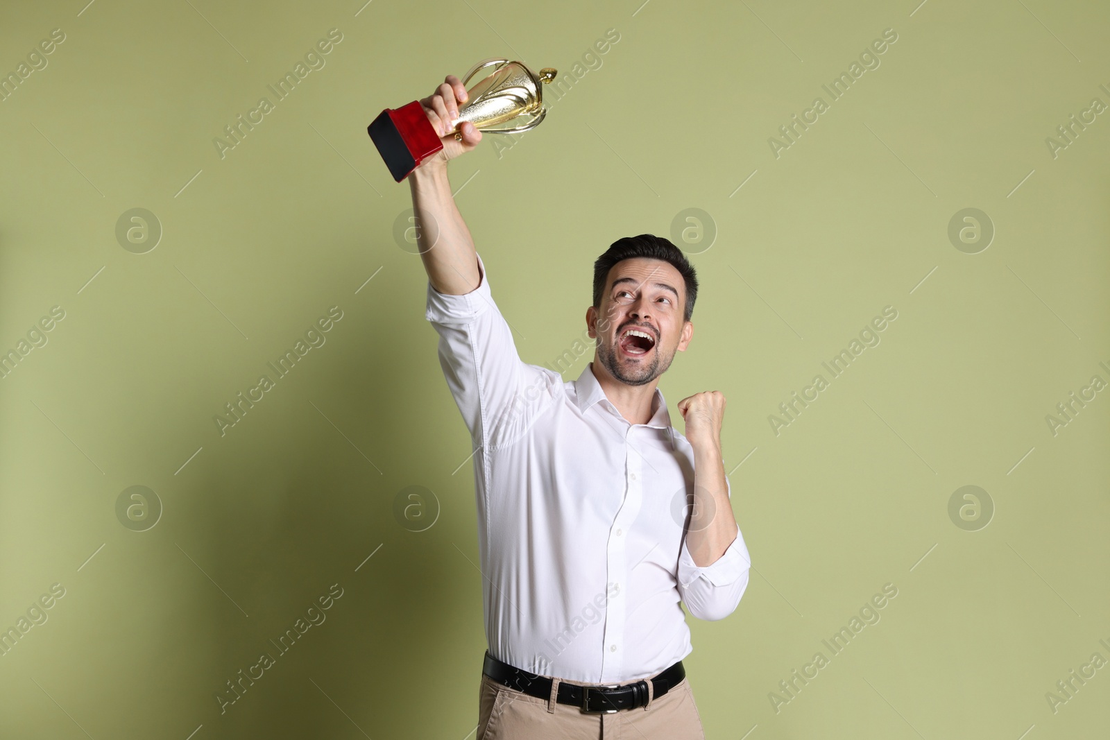 Photo of Happy winner with golden trophy cup on pale olive background