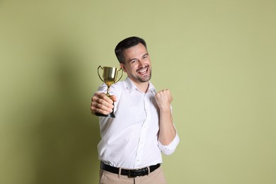 Photo of Happy winner with golden trophy cup on pale olive background