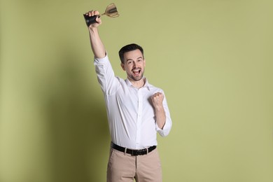 Photo of Happy winner with golden trophy cup on pale olive background