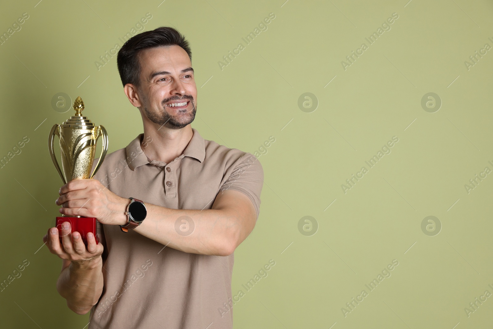 Photo of Happy winner with golden trophy cup on pale olive background, space for text