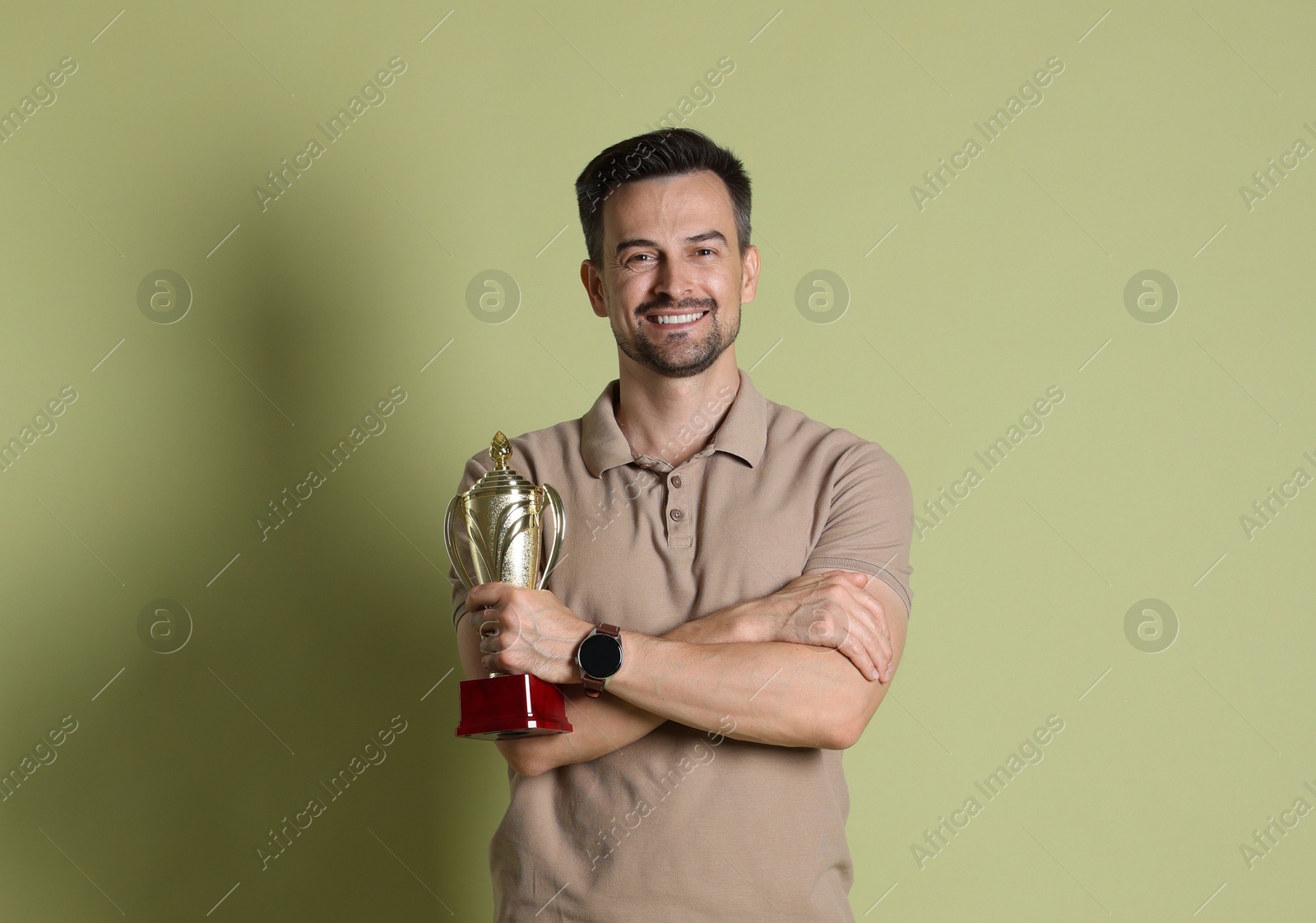 Photo of Happy winner with golden trophy cup on pale olive background