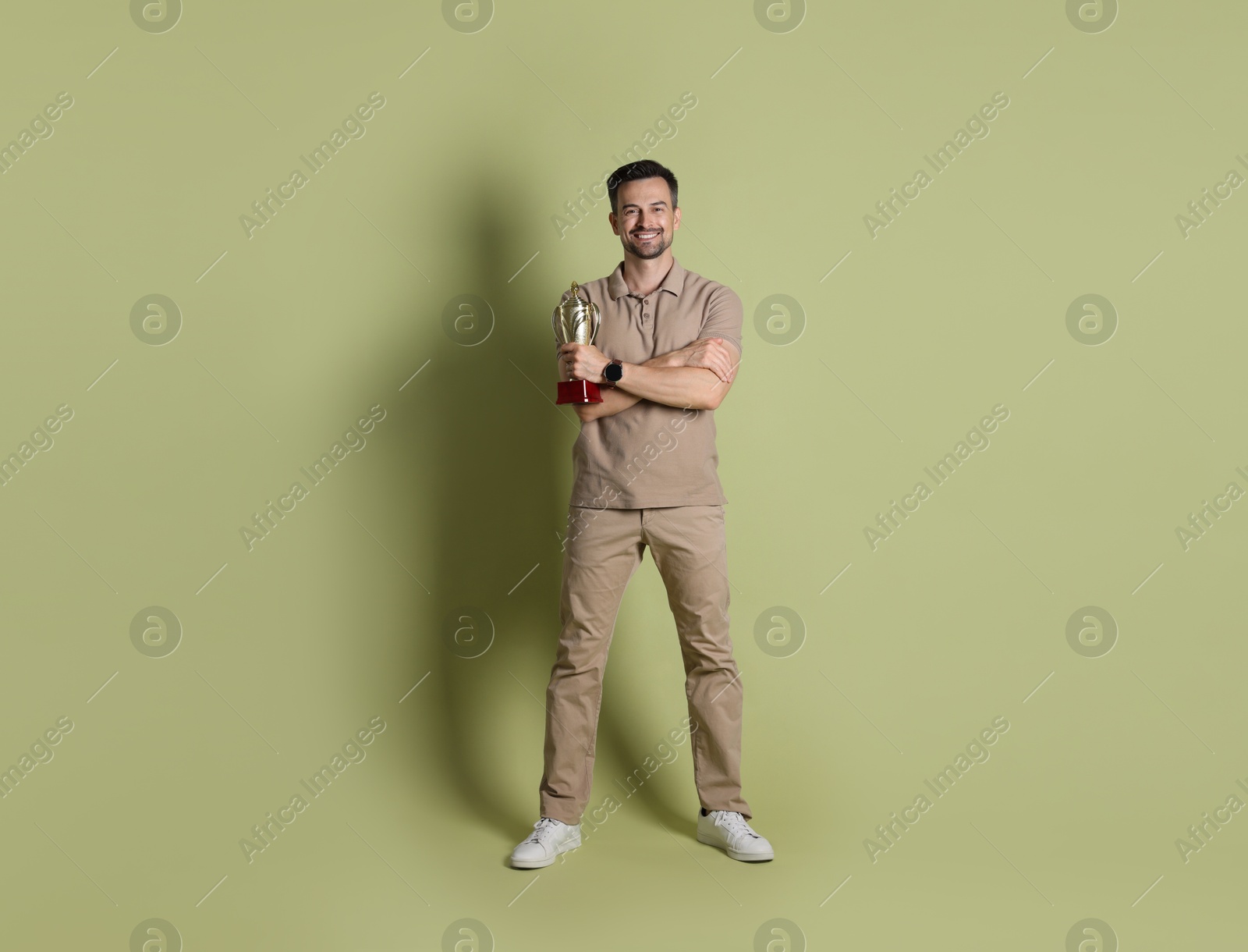 Photo of Happy winner with golden trophy cup on pale olive background