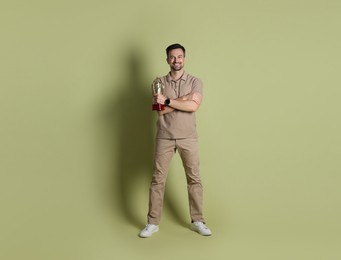 Happy winner with golden trophy cup on pale olive background