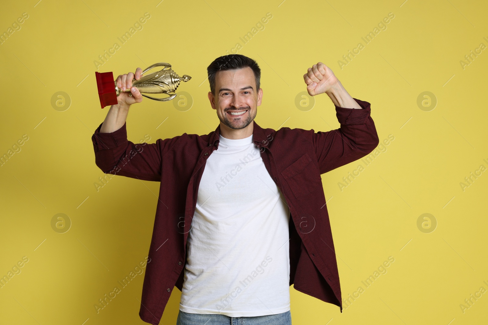 Photo of Happy winner with golden trophy cup on yellow background