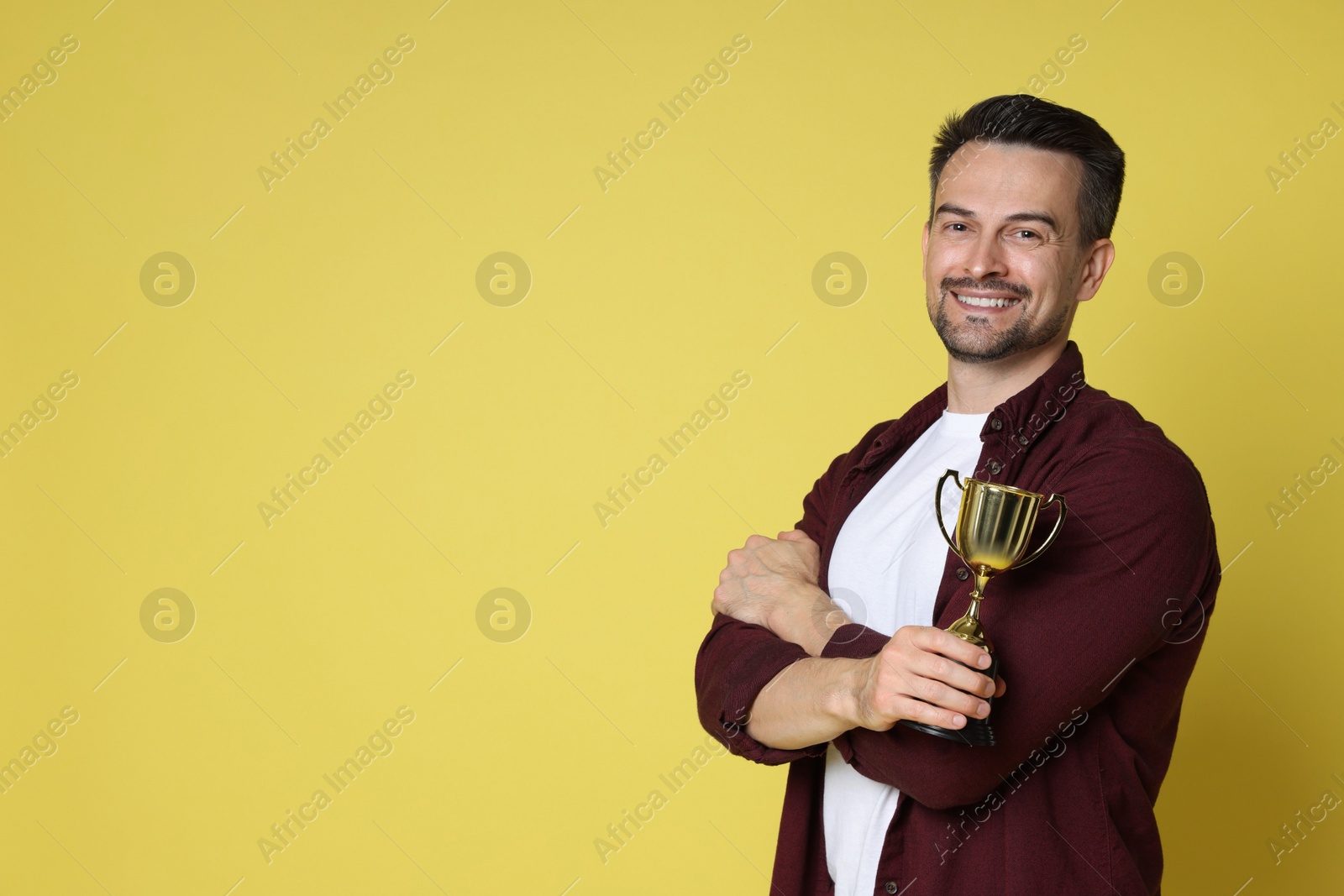 Photo of Happy winner with golden trophy cup on yellow background, space for text