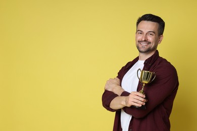 Photo of Happy winner with golden trophy cup on yellow background, space for text