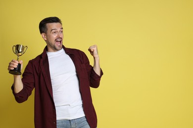 Happy winner with golden trophy cup on yellow background, space for text