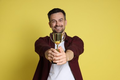 Photo of Happy winner with golden trophy cup on yellow background