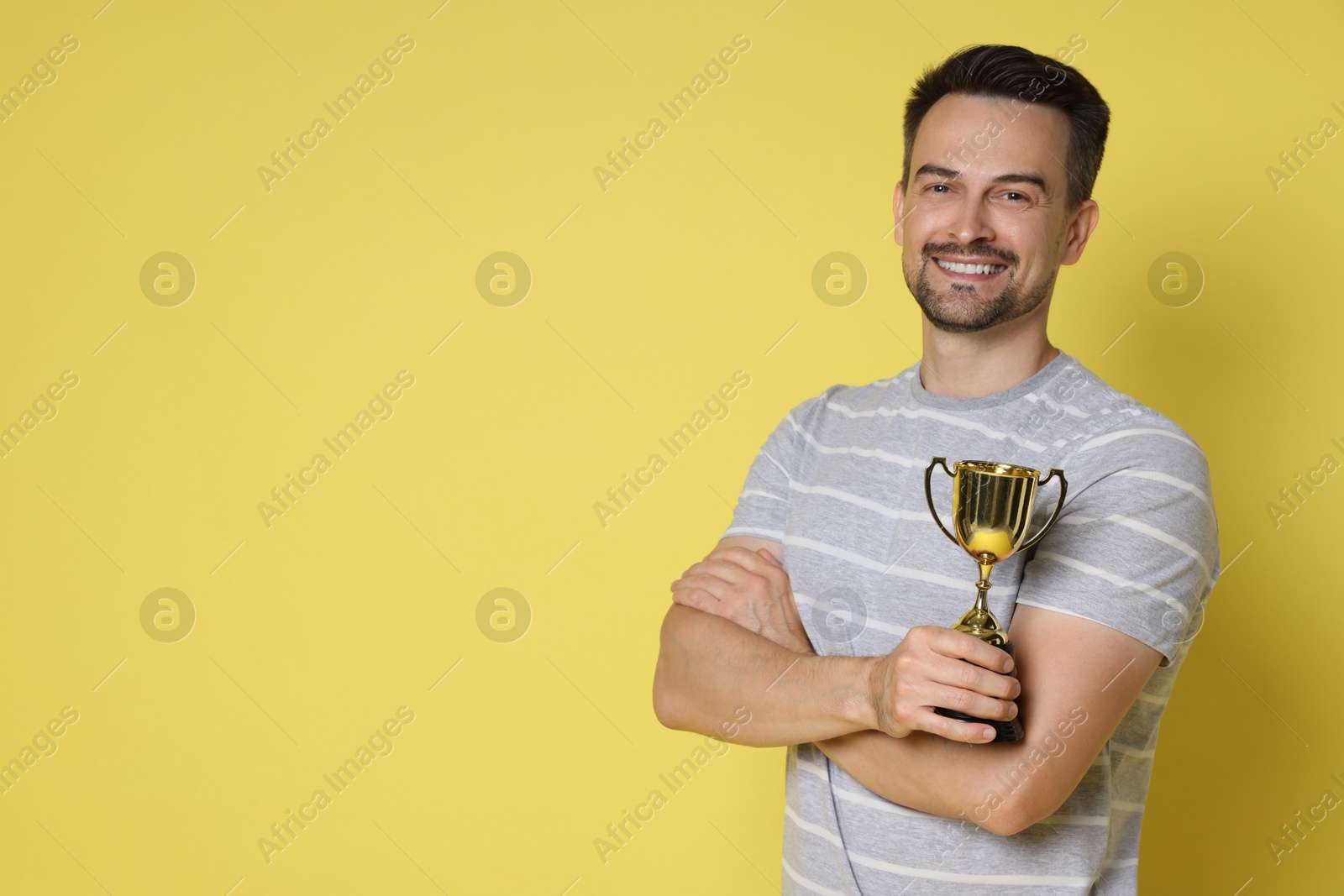 Photo of Happy winner with golden trophy cup on yellow background, space for text