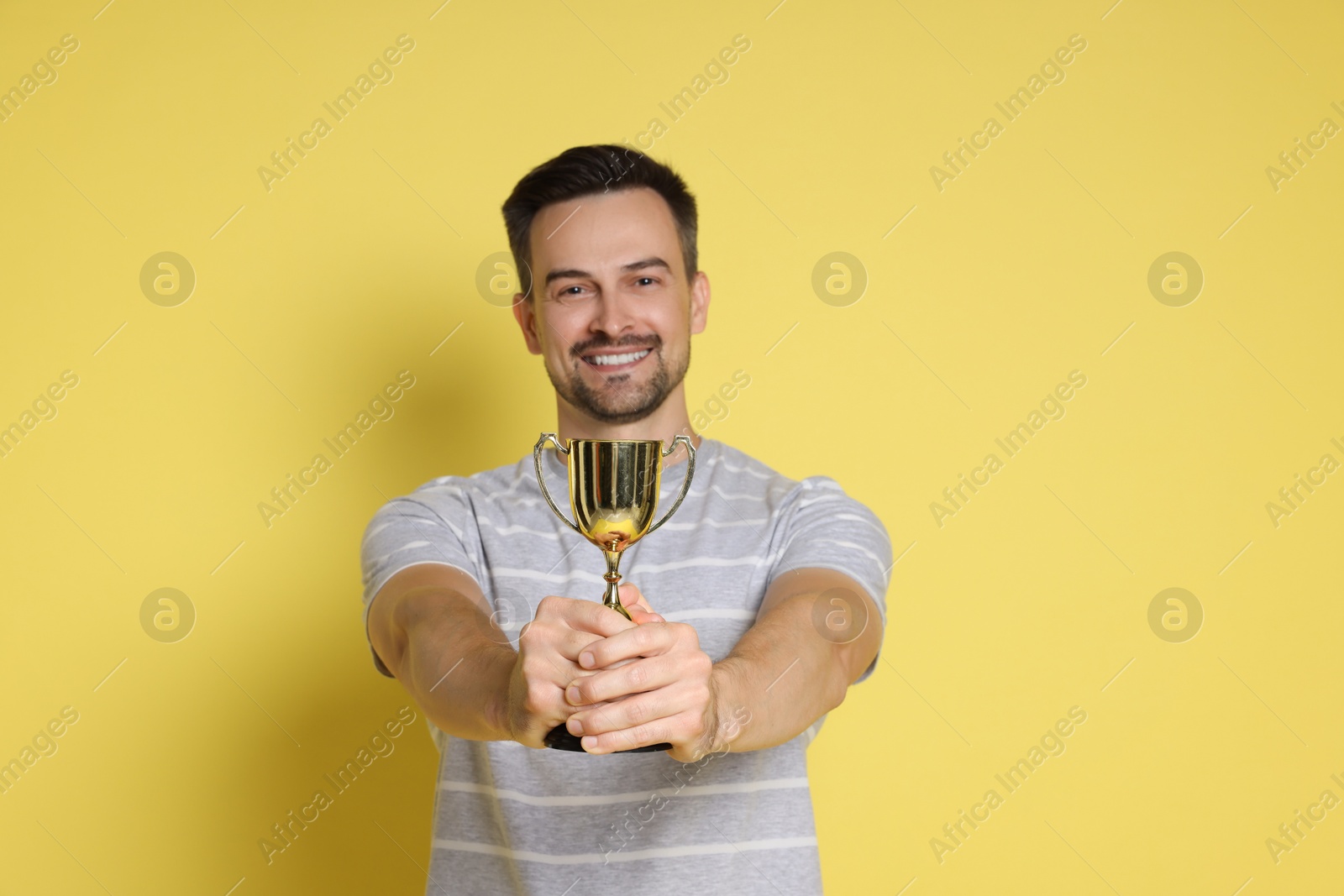 Photo of Happy winner with golden trophy cup on yellow background