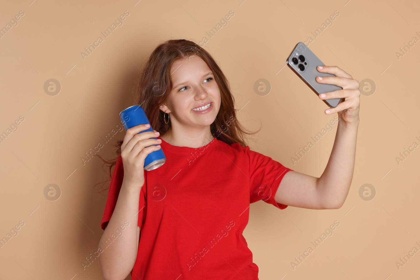 Photo of Smiling teenage girl with can taking selfie on beige background