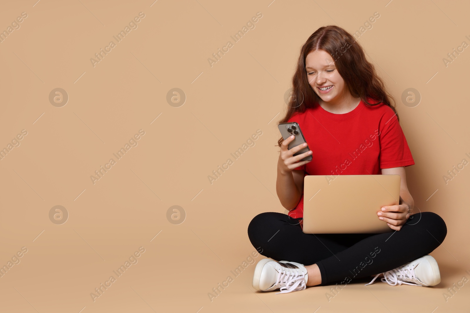 Photo of Smiling teenage girl with laptop and smartphone on beige background. Space for text