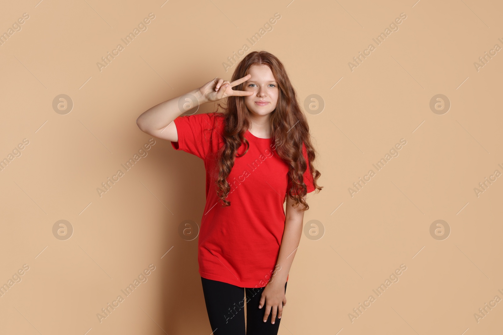 Photo of Cute teenage girl showing peace sign on beige background