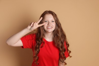 Photo of Smiling teenage girl showing peace sign on beige background