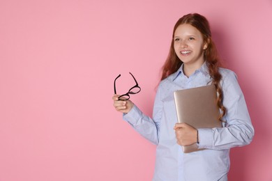 Smiling teenage girl with laptop and glasses on pink background. Space for text