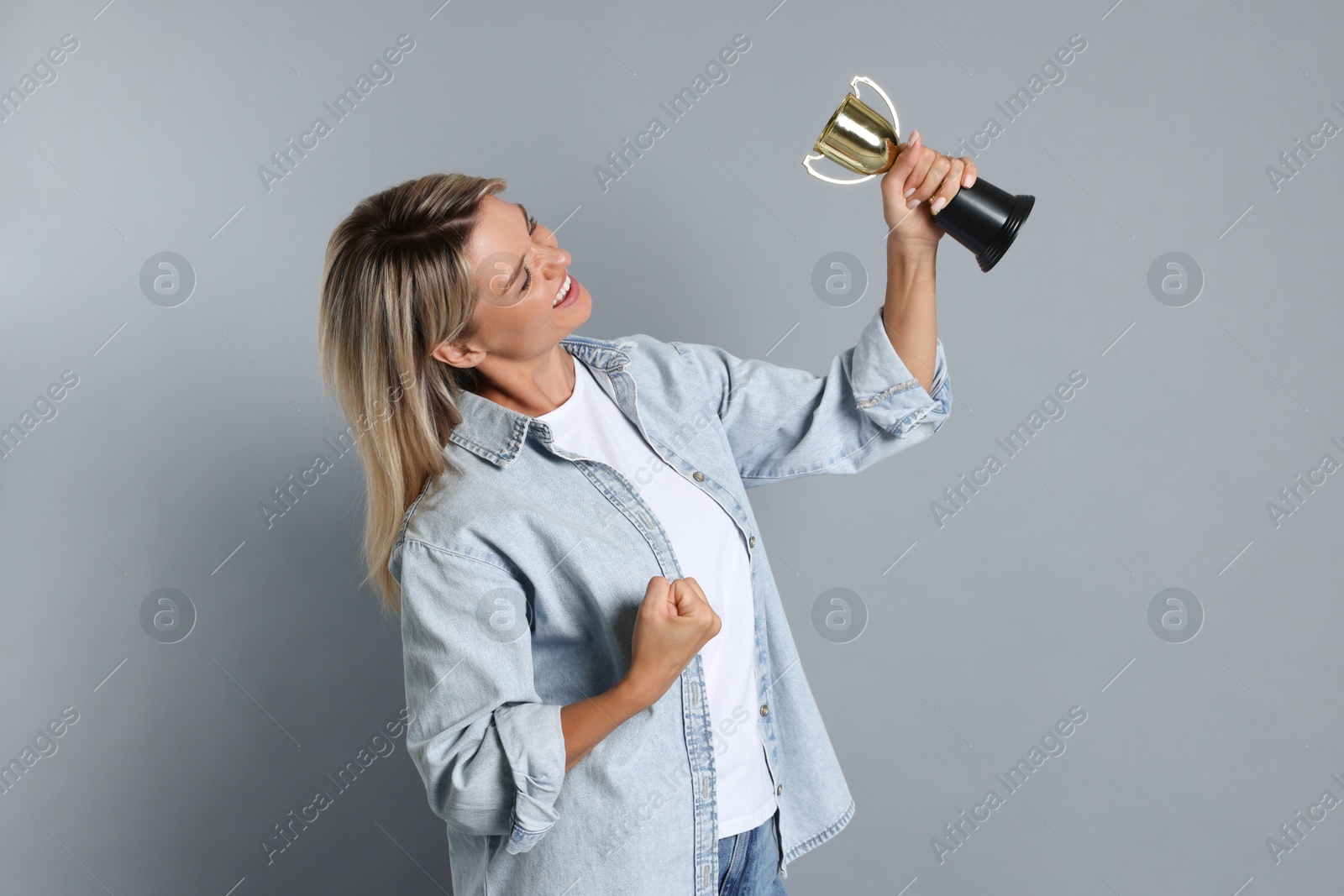 Photo of Happy winner with golden trophy cup on gray background