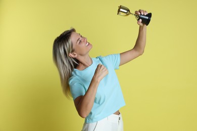 Photo of Happy winner with golden trophy cup on yellow background