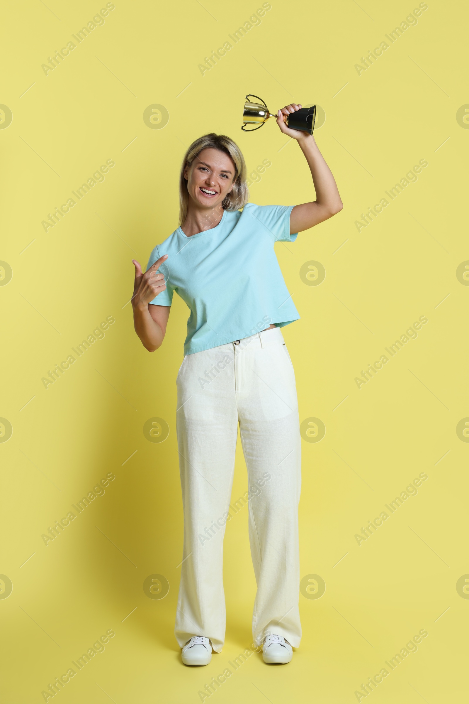 Photo of Happy winner with golden trophy cup on yellow background